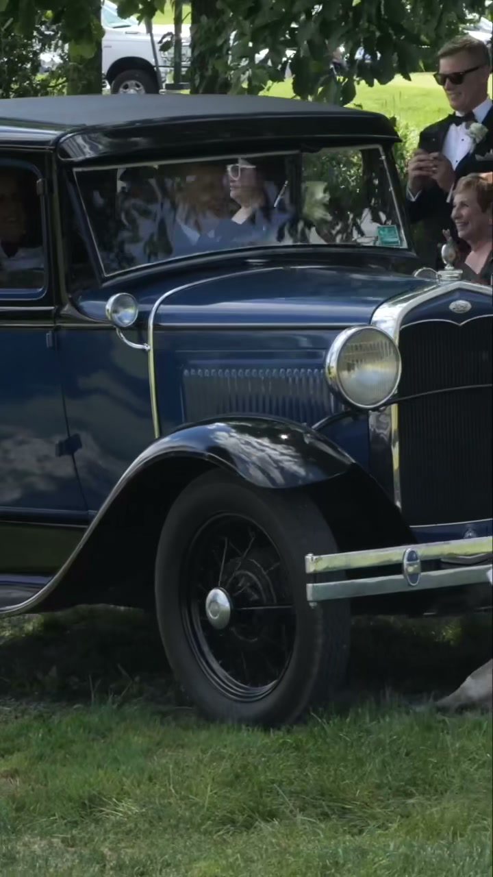Bride and groom waving from vintage antique car